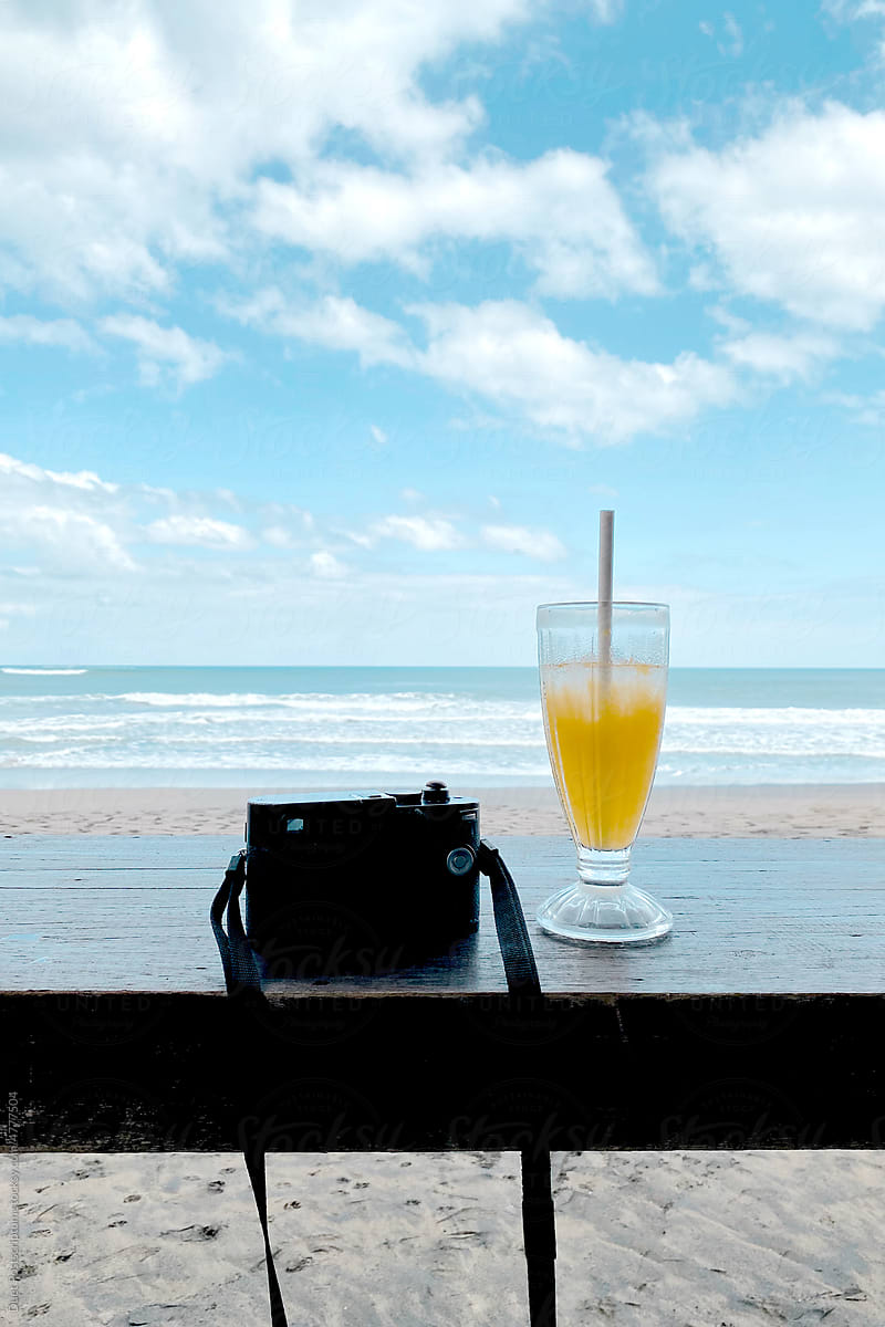 Camera and a glass of orange juice on the background of the coast