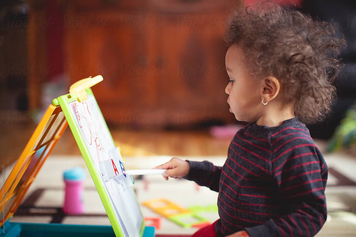 Toddler child drawing happily on her toy easel