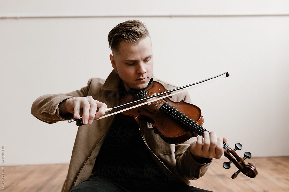 young stylish man sitting on studio floor playing violin