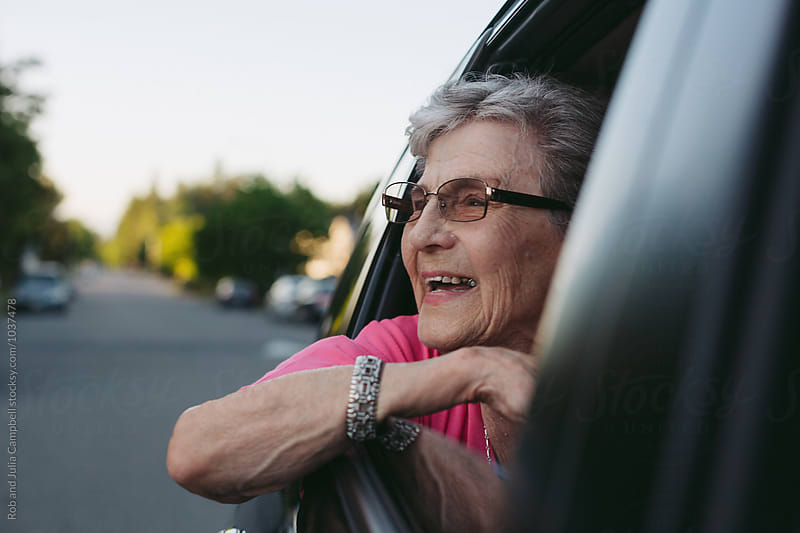 Happy, excited caucasian senior woman leaning out moving car window