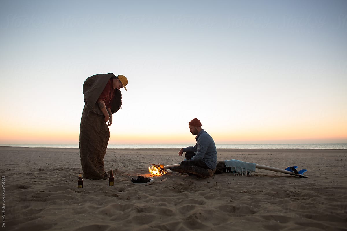 Two friends camping on the beach next to a bonfire.