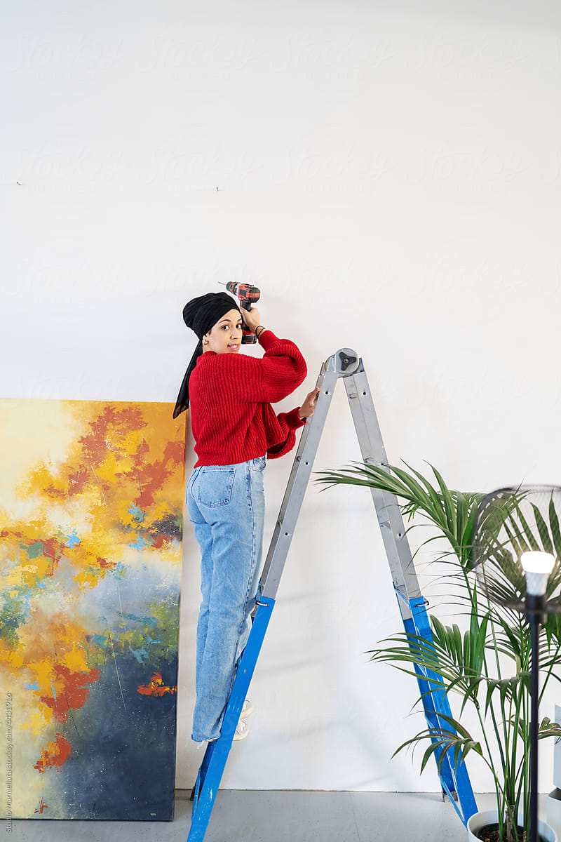 Arab female on ladder drilling hole on wall