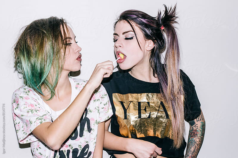 two fashionable tattooed girls with colorful hairstyles  eat candy,direct light