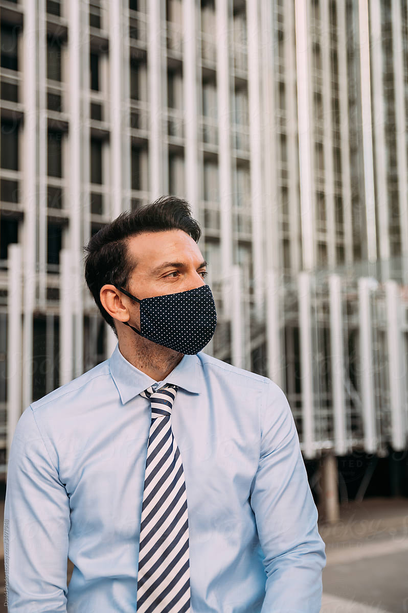 Businessman in protective mask looking away in city