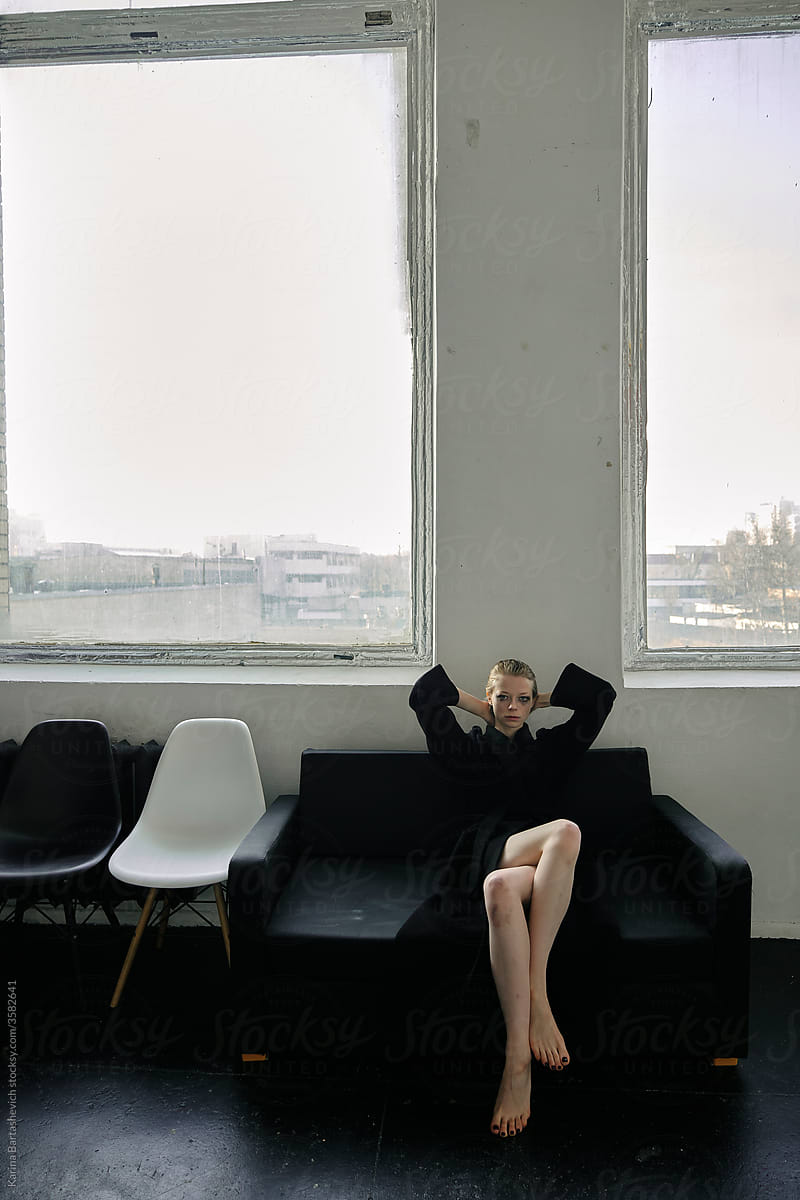 artistic photo of a girl sitting against the background of large windows, elegantly throwing her legs over her legs
