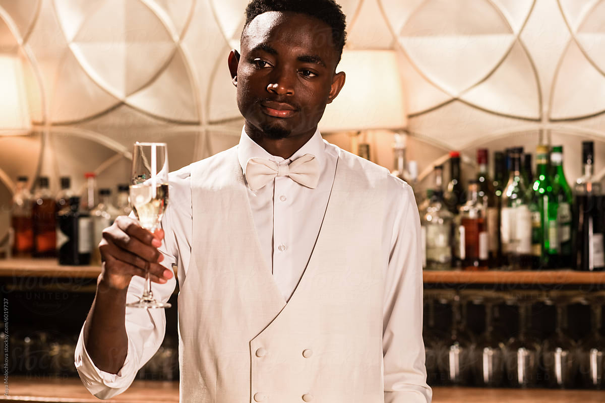 Young stylish bartender holds out a glass of champagne to the client