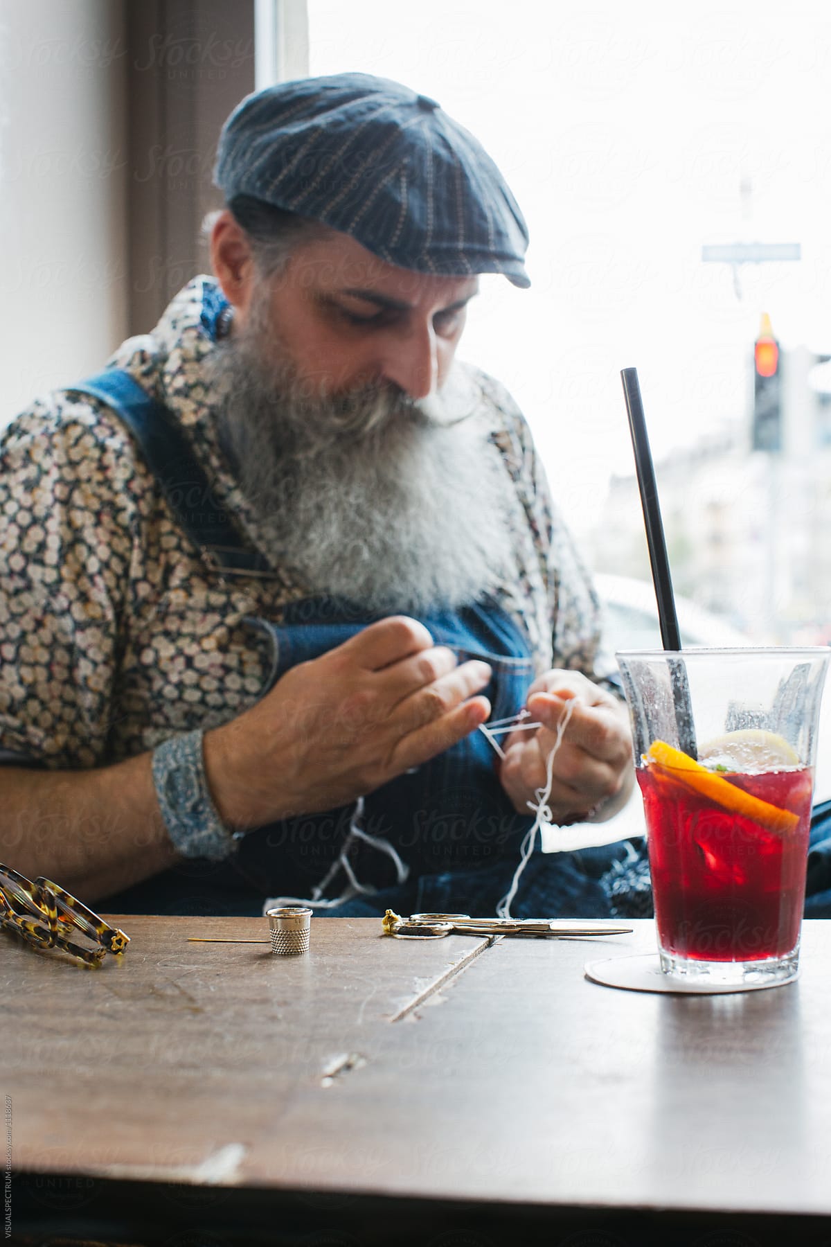 Indoor Portrait of Cool Elderly Male Hipster Sewing in Bright Restaurant