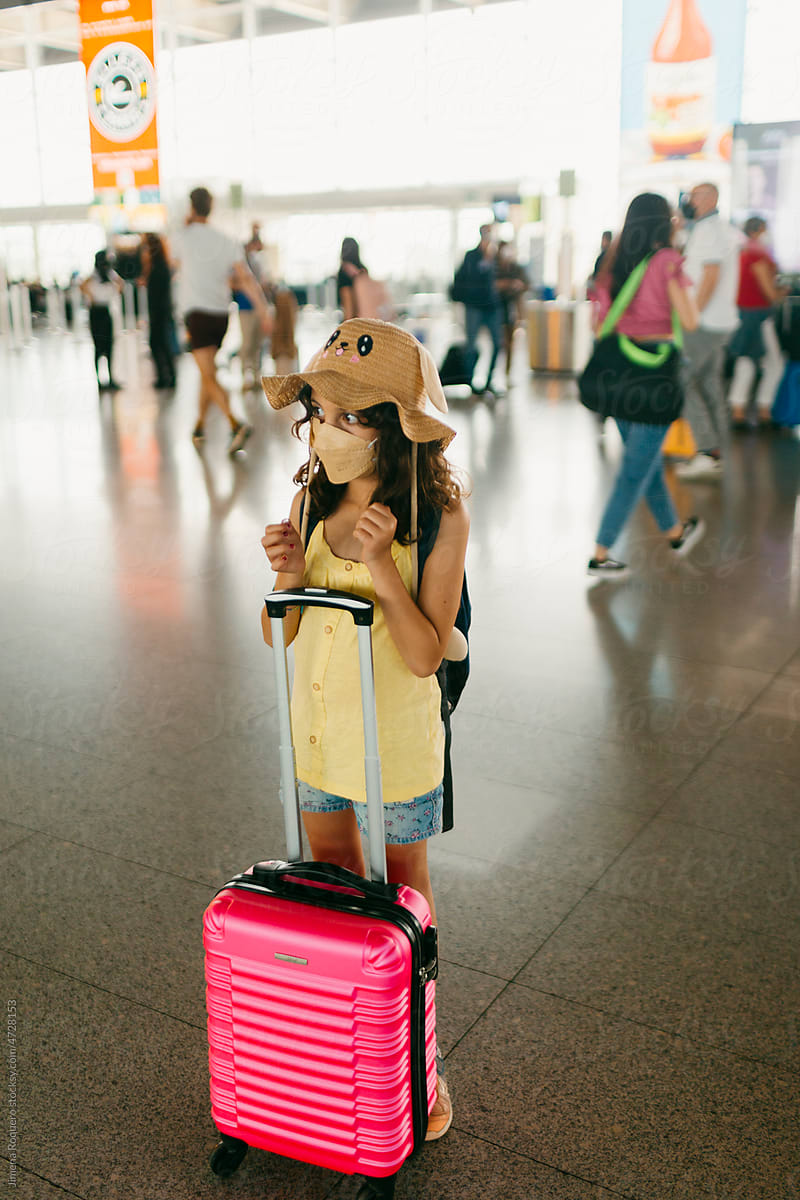 kid with funny hat and face-mask standing with luggage in airport