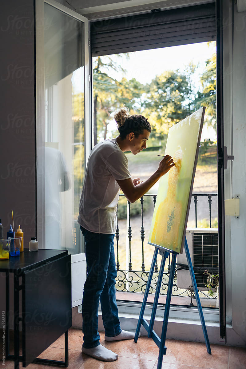 Artist painting a canvas near a balcony in a studio