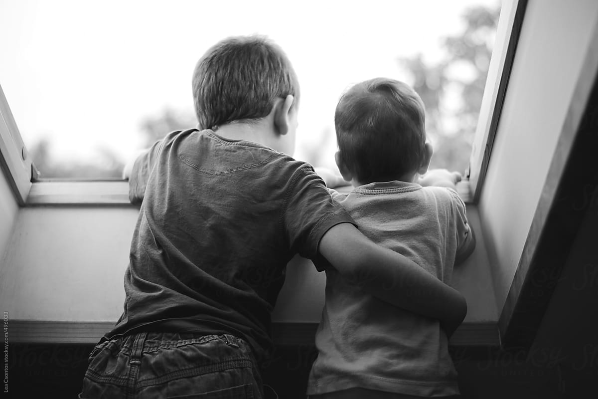 Young brother holding his sister protectively while looking out of a window.