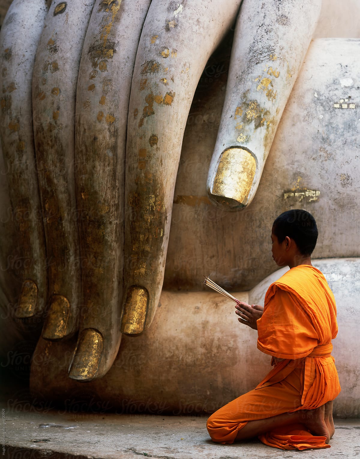 Buddhist Monk Praying Infront Of The Wat Si Chum Seated Buddha Thailand By Stocksy