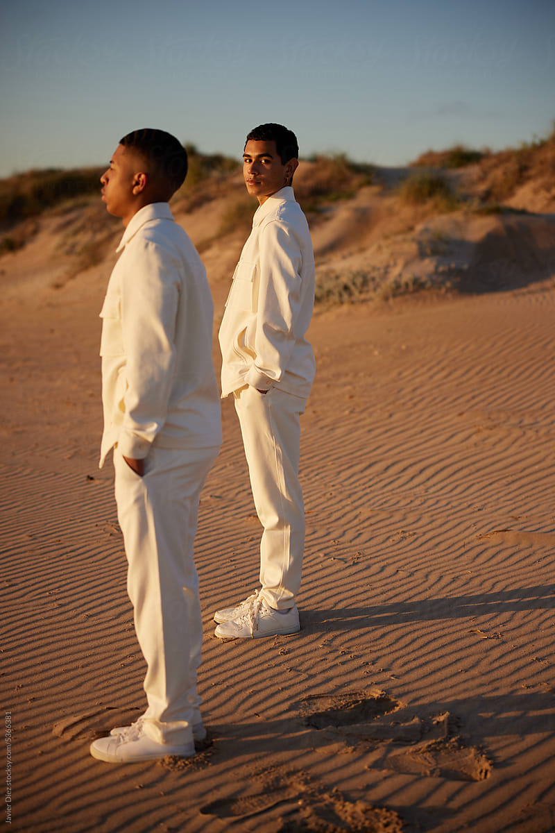 Stylish male models in white outfits standing in desert