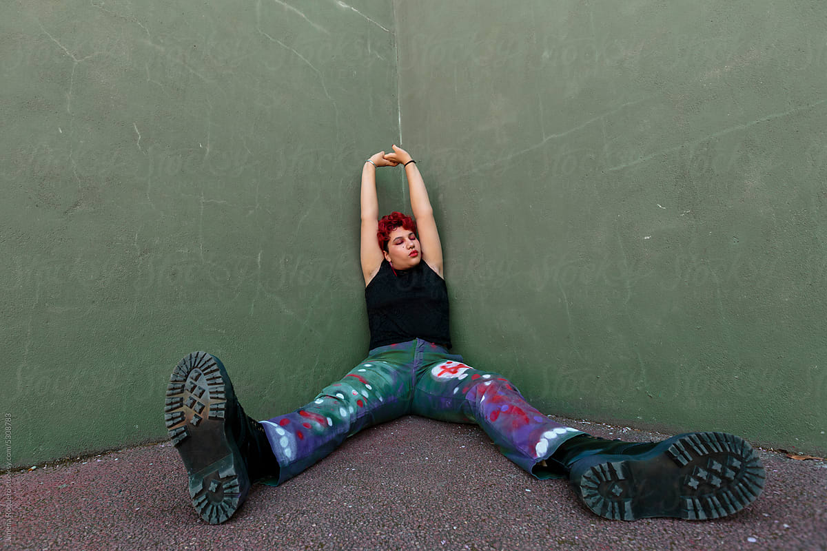 Non-binary person sitting on ground over green wall stretching arms