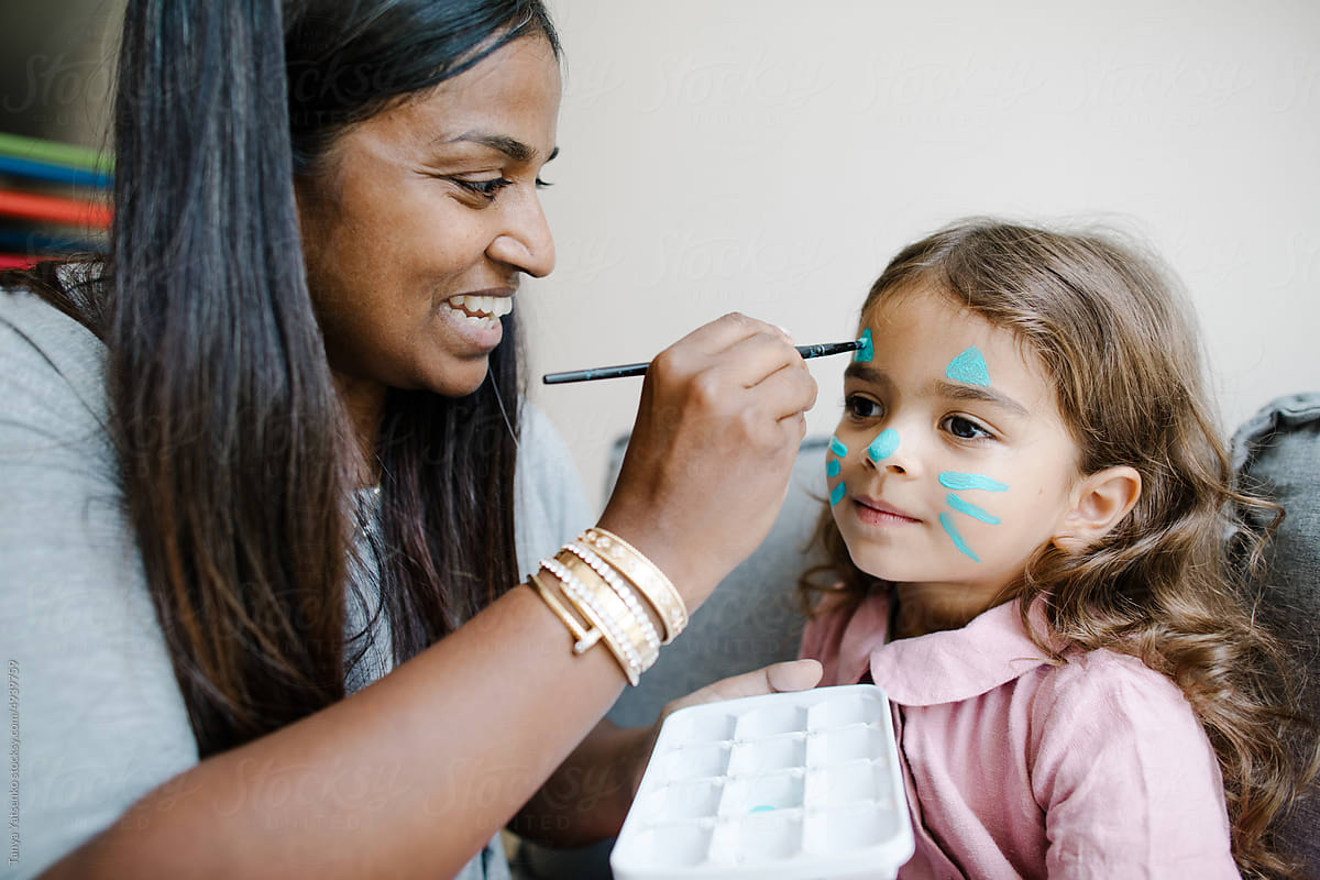 Woman paint a daughter\'s face with blue paint