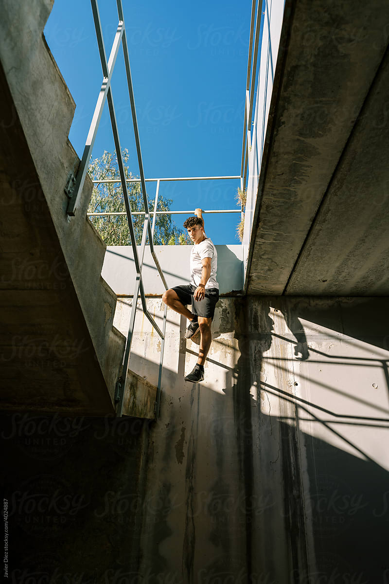Young man hanging on railing of urban building