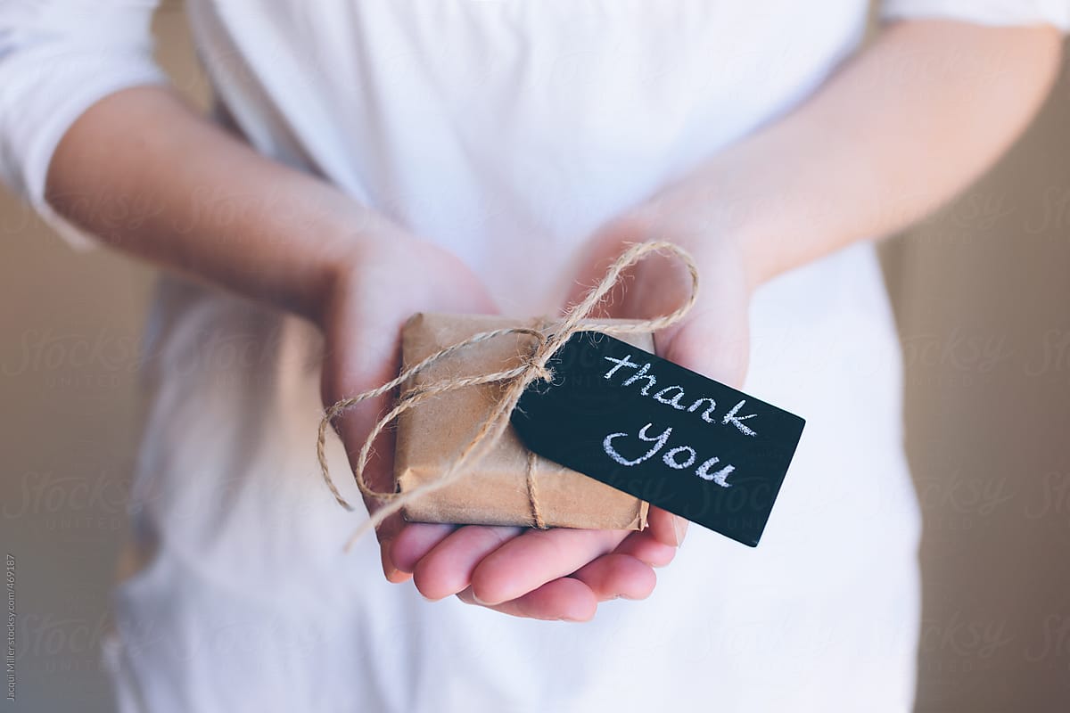 Girls hands holding a small gift wrapped in brown paper with a tag that says \'thank you\'