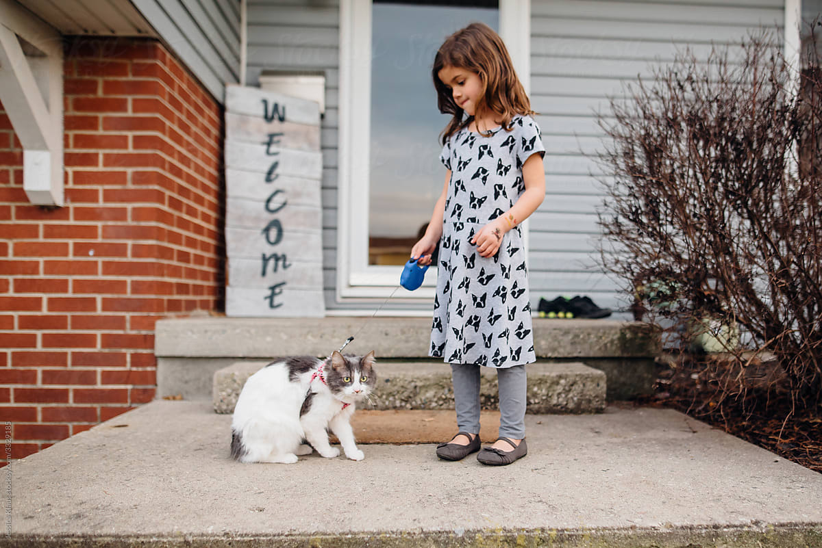 Young girl walking white and gray cat on leash.