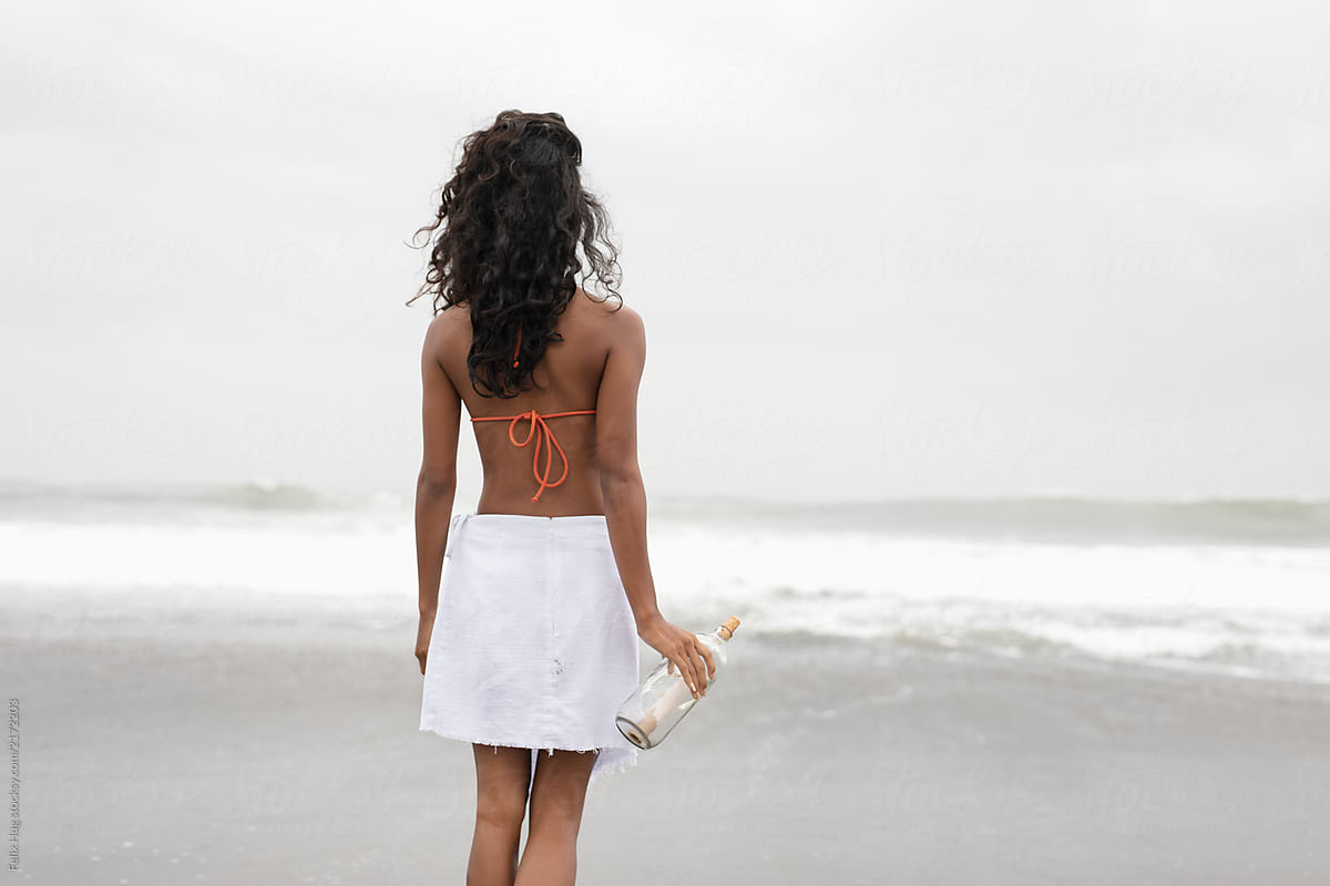 A Young asian woman holds a bottle with a  message looking out to the ocean
