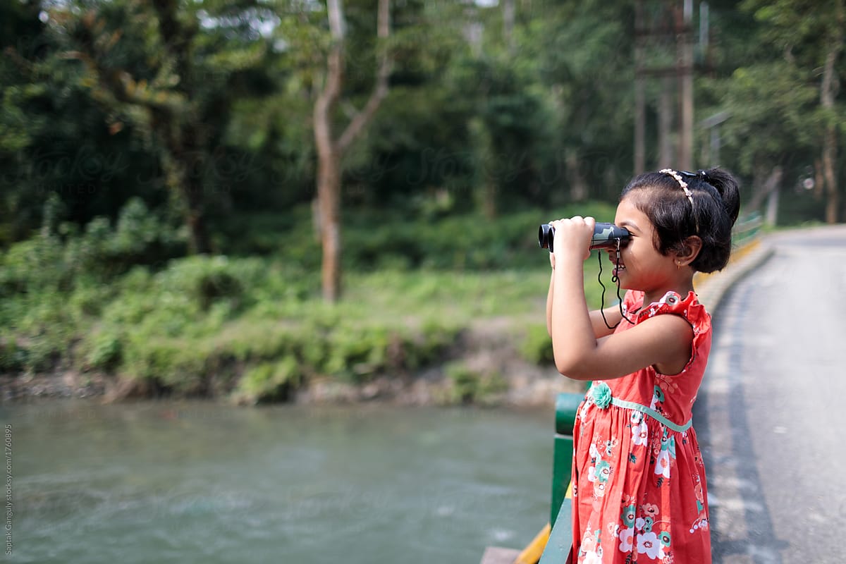 Little girl looking through a binocular in the forest