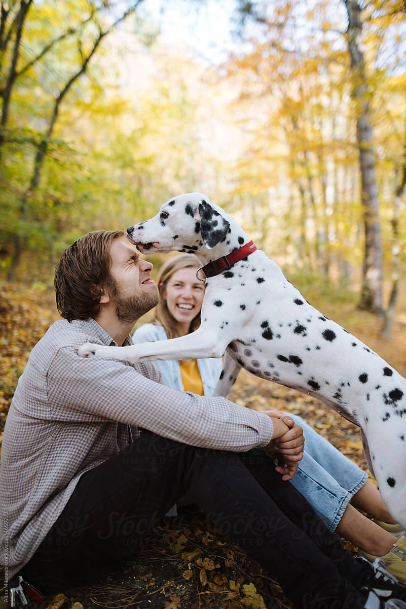 Young couple having fun with dog in autumn park