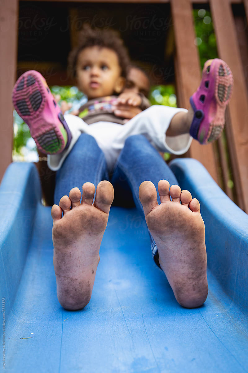 Child with muddy feet using a slide with her sister