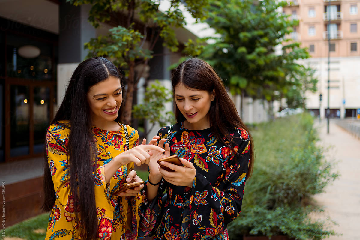 Happy girlfriends using a smartphone in town