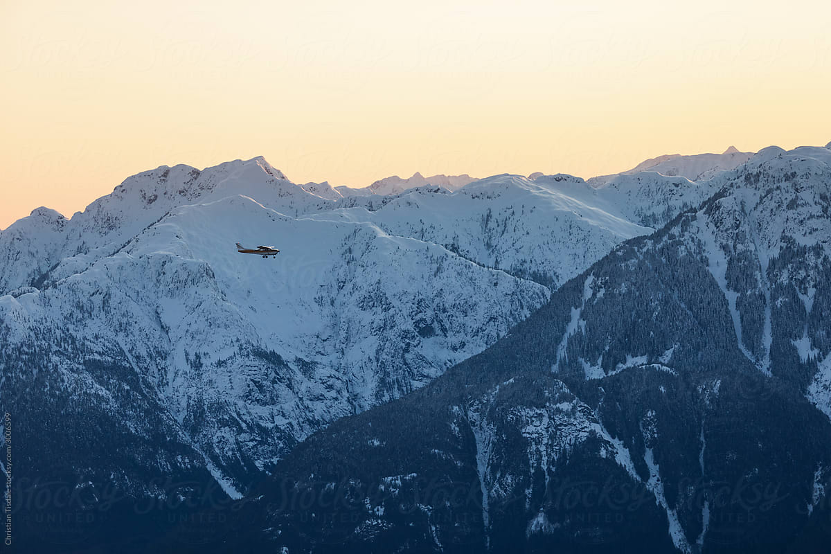 A single engine airplane flying through snowy mountains at sunset