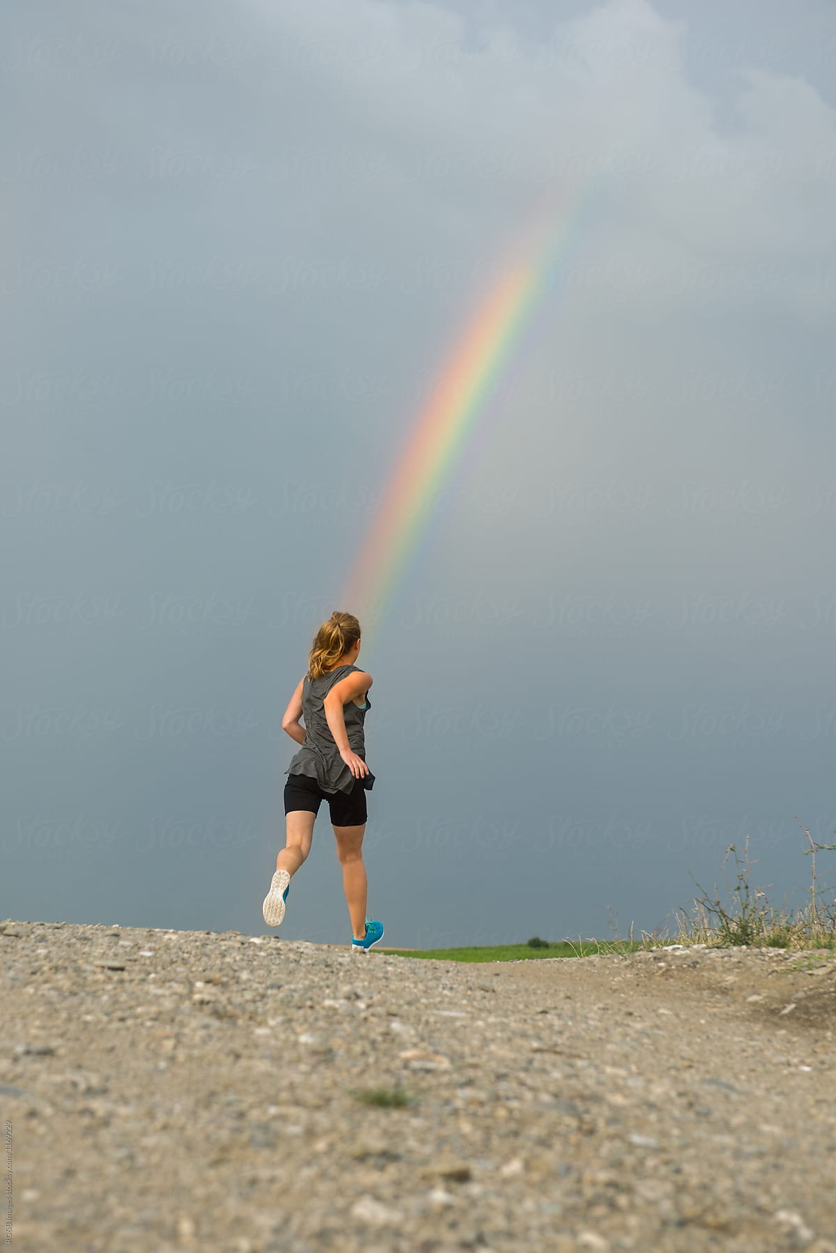 Young woman running towards the rainbow on a cloudy day