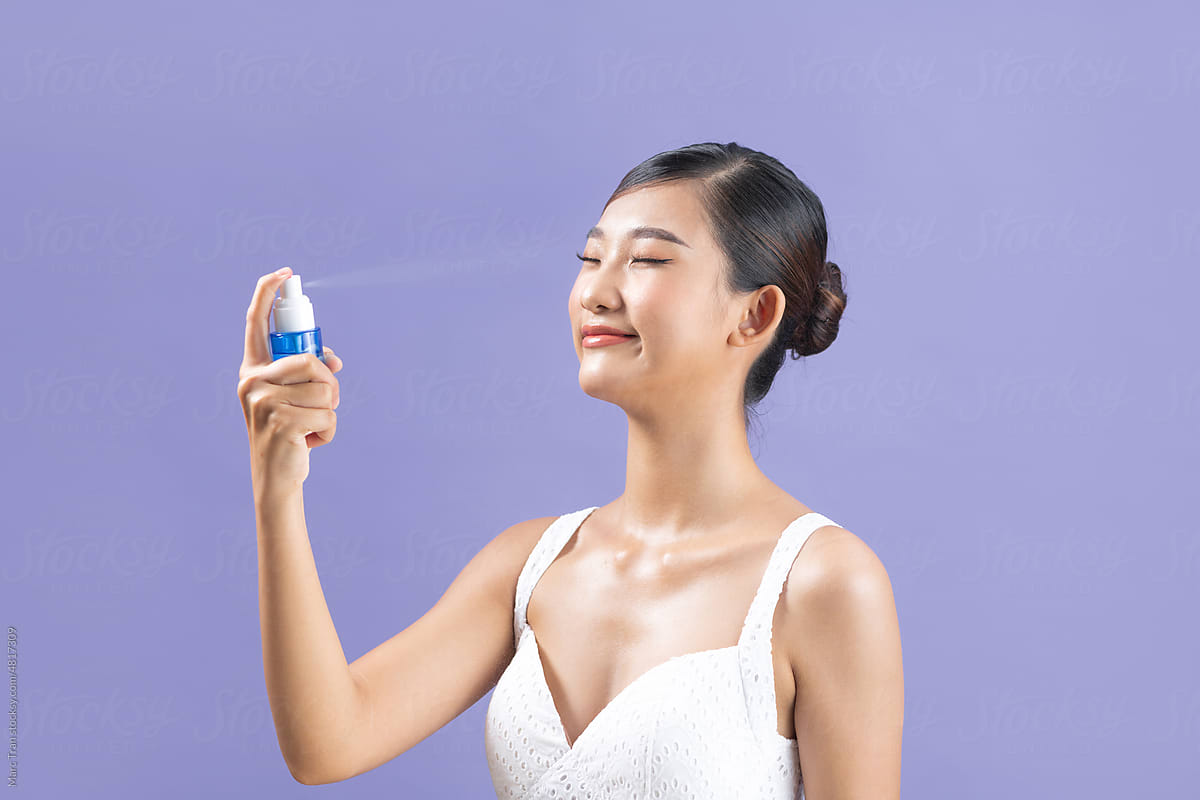 Side view of a pleased young Asian woman spraying thermal water