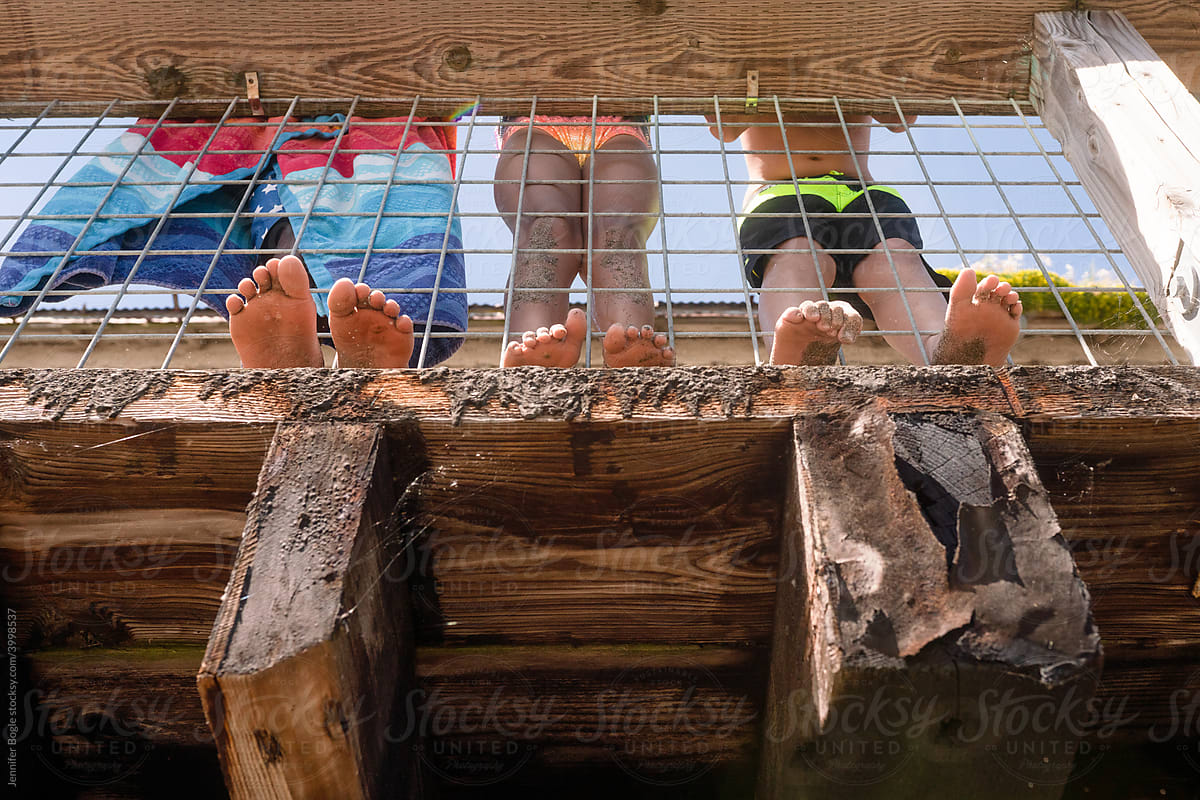 Children\'s sandy feet stick through rail of dock