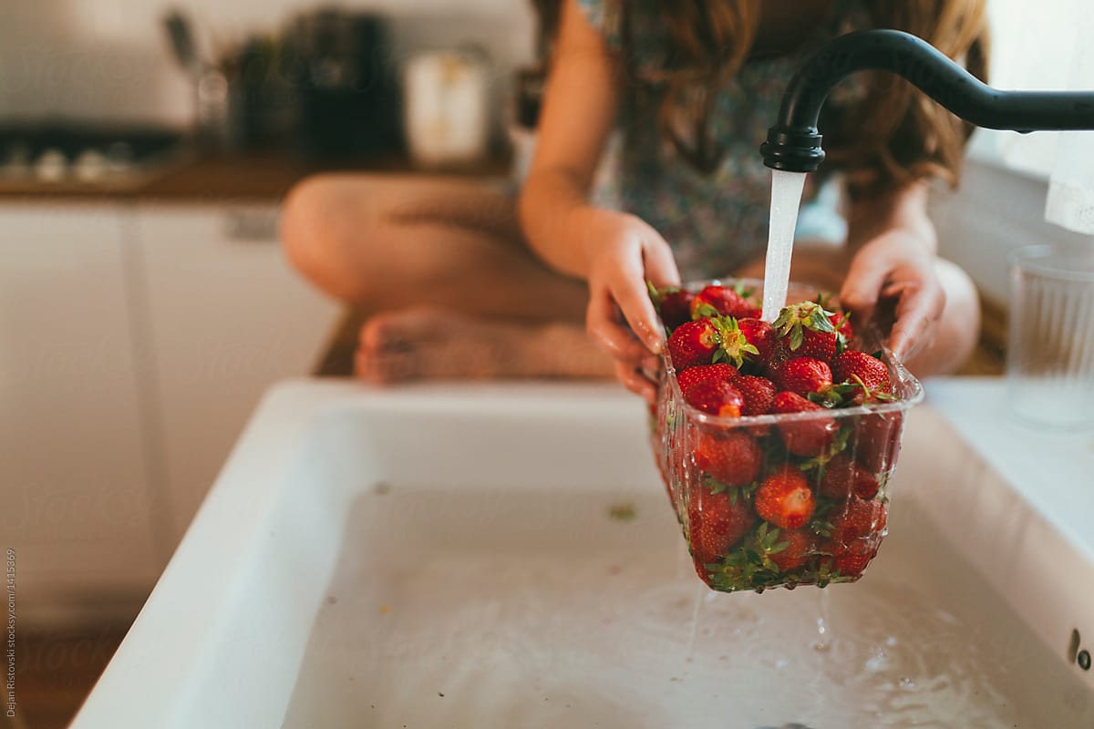 Girl washing strawberries in the kitchen.