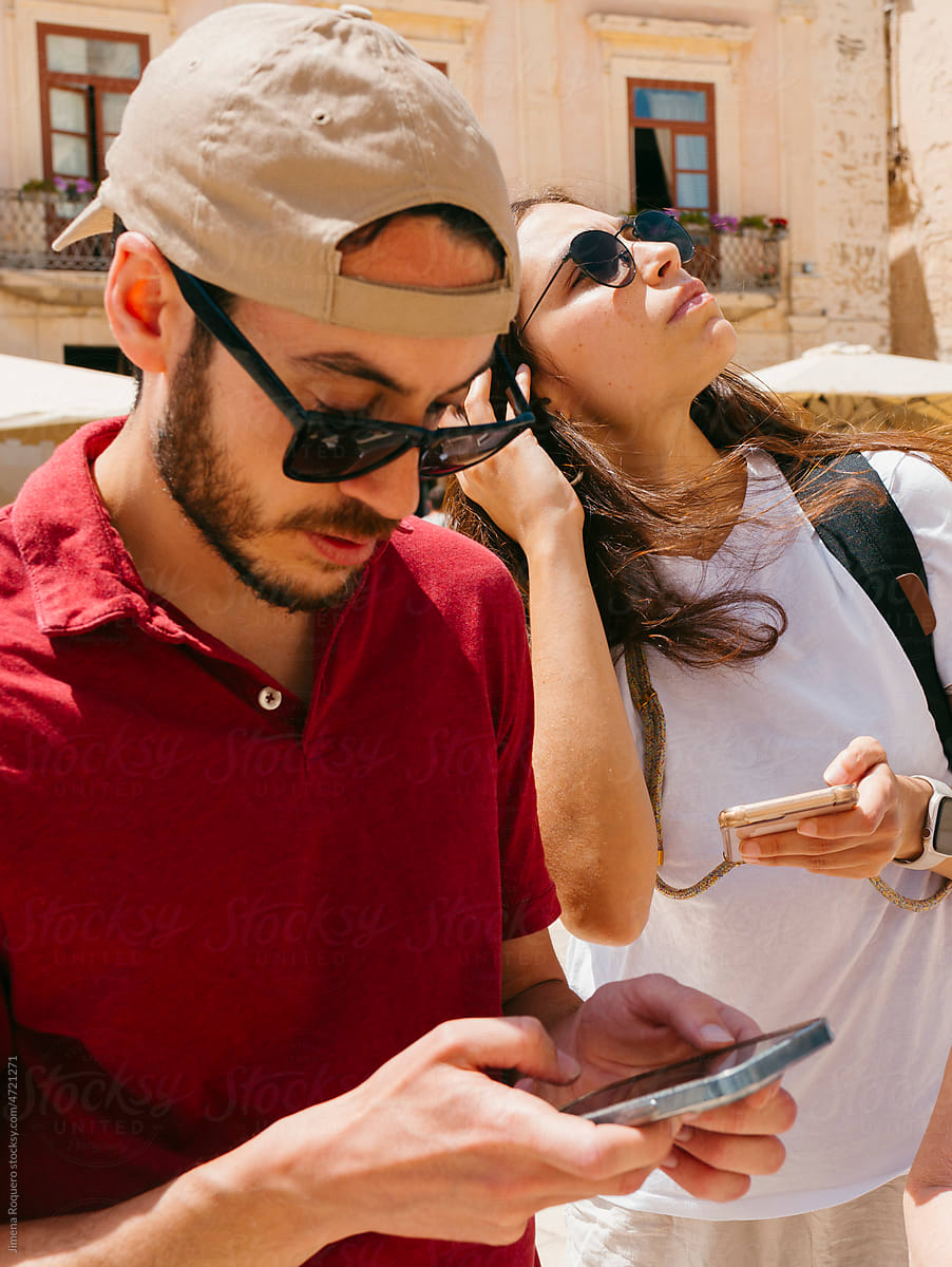 Tourists with sunglasses checking their smartphones in sunlight