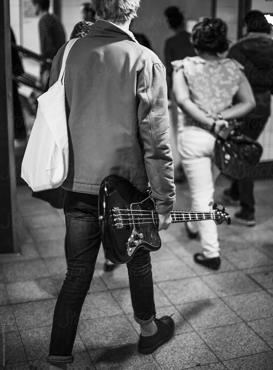 Punk Rocker man walking in the subway holding a bass guitar