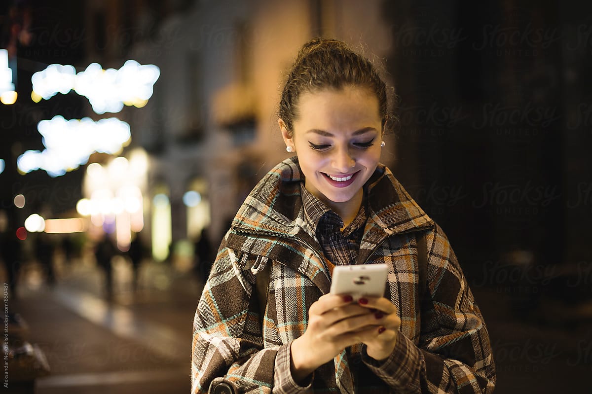 Beautiful woman texting on her smartphone by night, outdoors