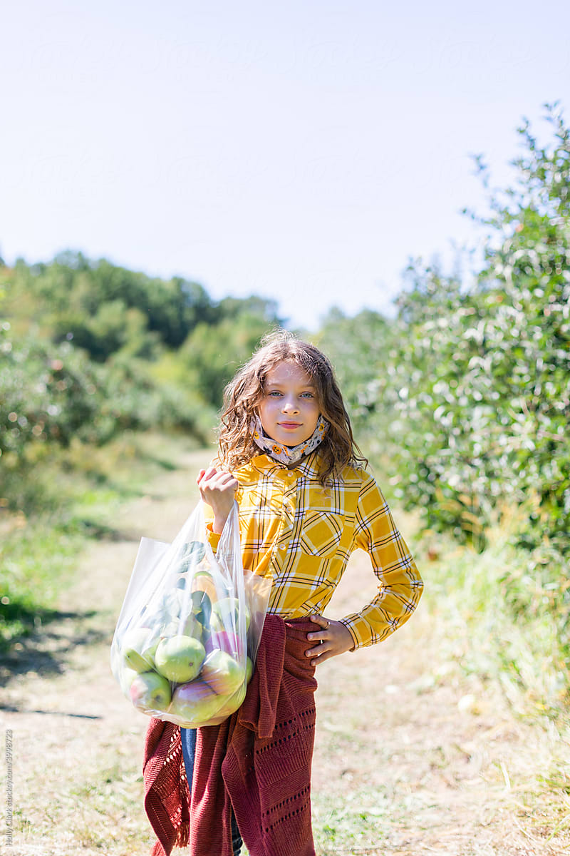 Portrait of blond girl holding full bag of ripe apples.