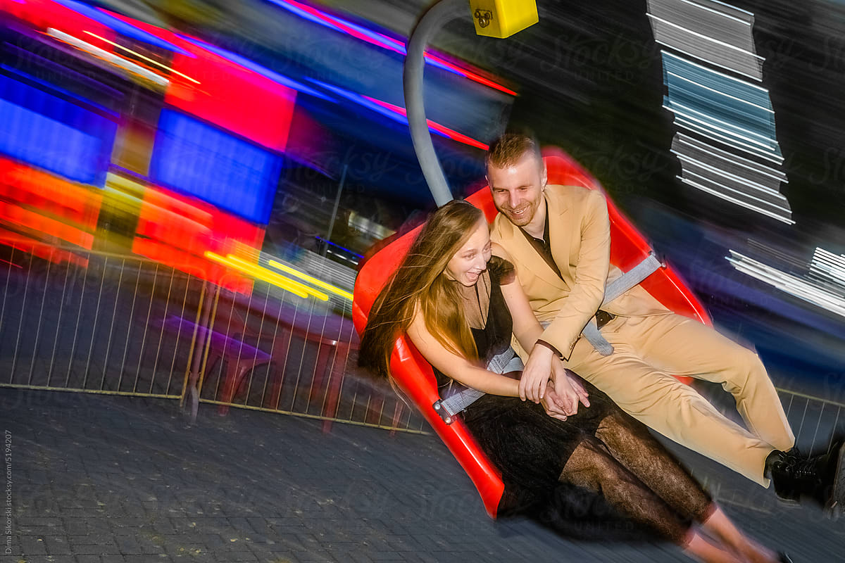An enthusiastic joyful couple in love rides at night on an attraction