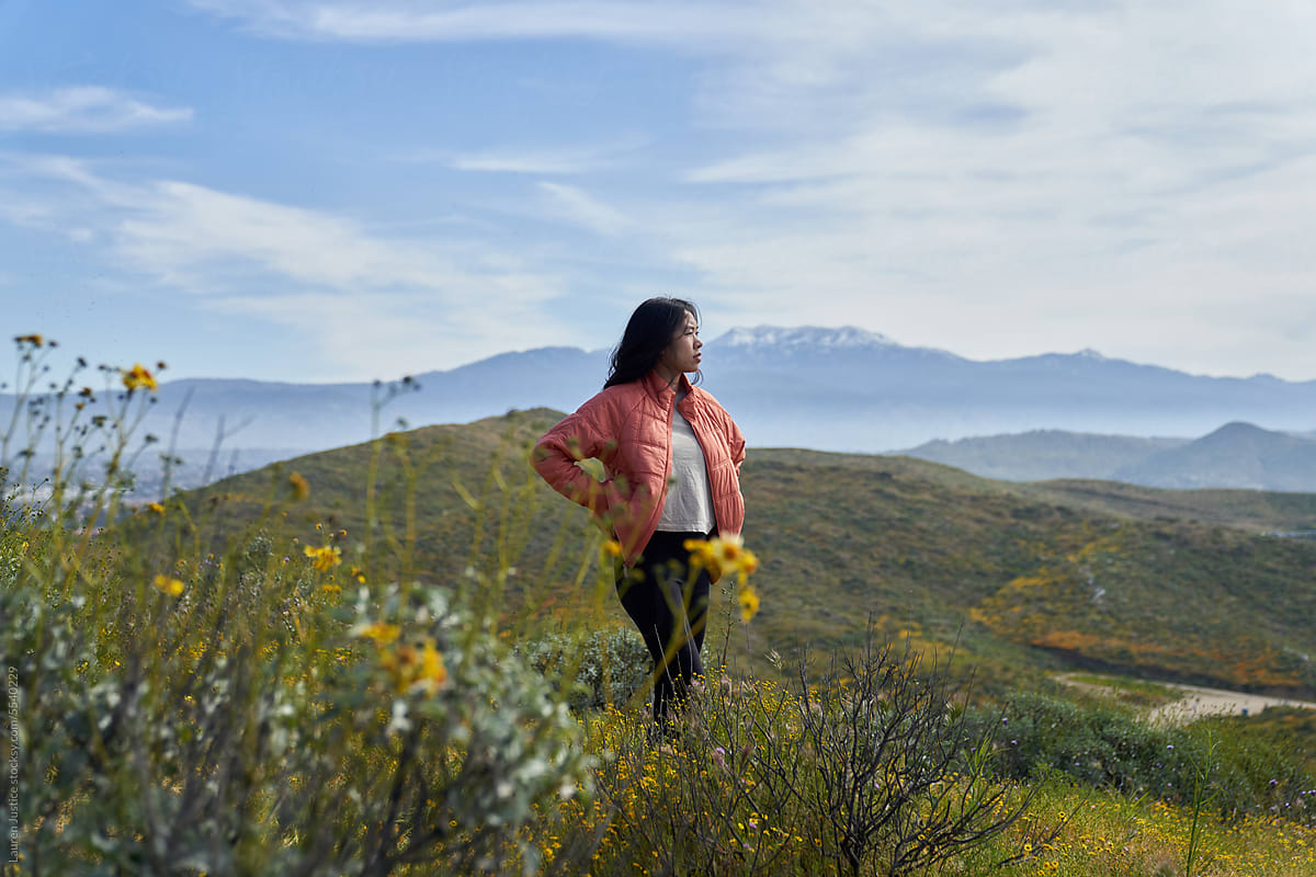 An asian girl looks out across a field of flowers and mountains