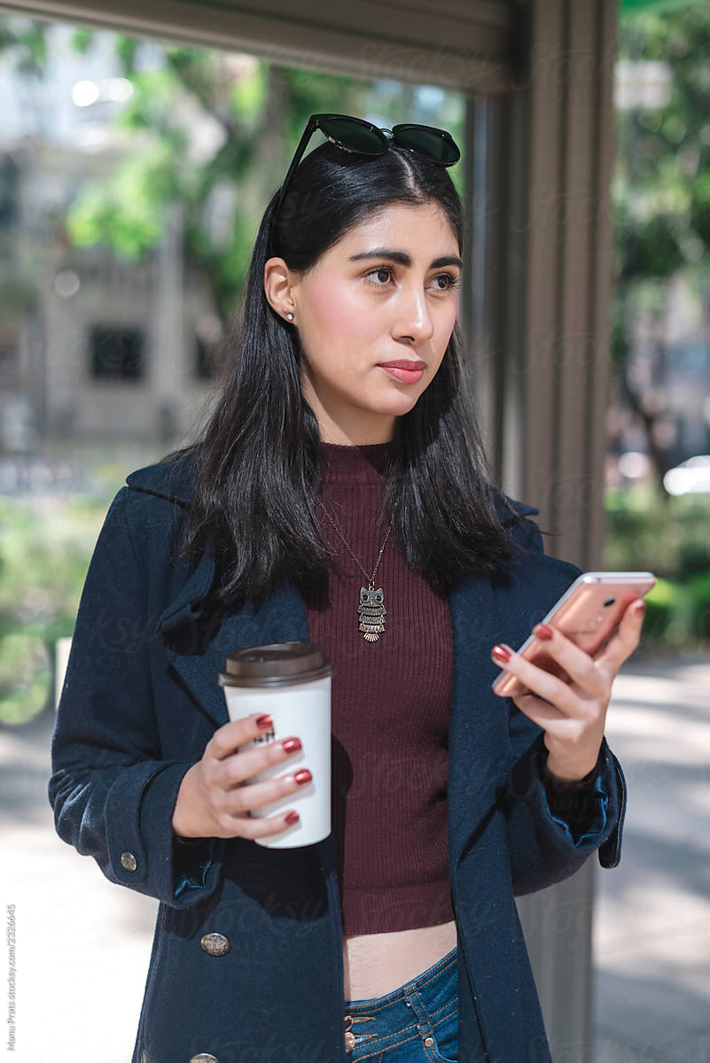 Hispanic woman using phone at bus stop