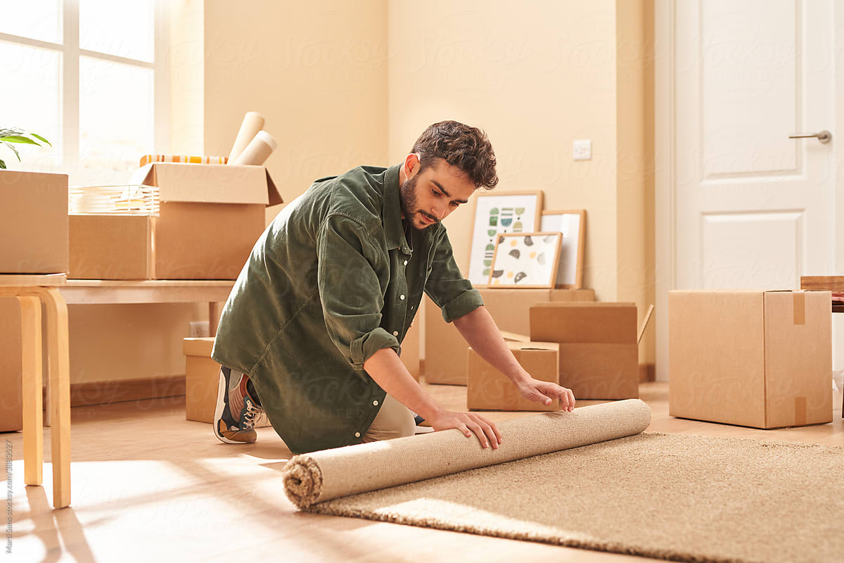 Young man unrolling carpet in light room