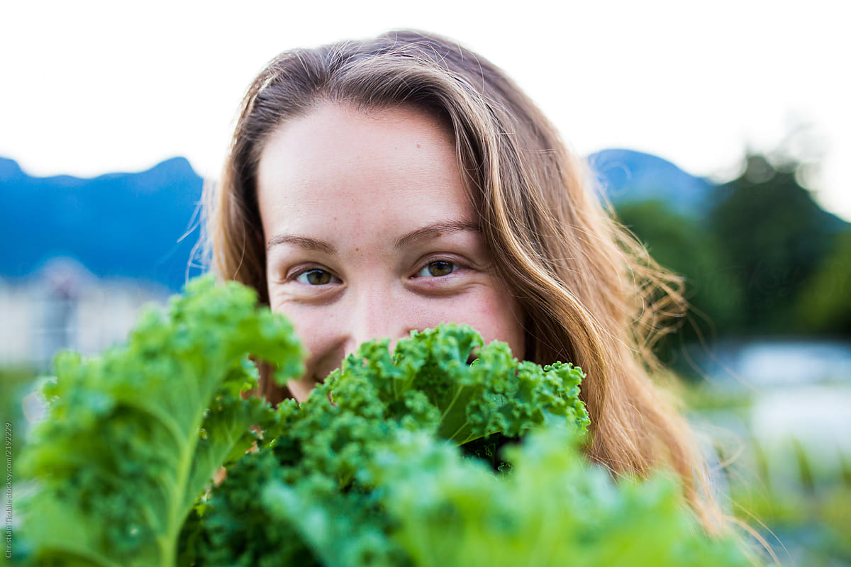 Young woman smiling behind a bundle of freshly picked vegetables