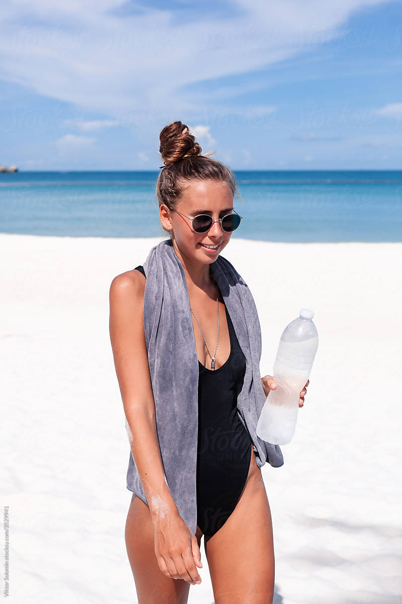 Woman in swimsuit and with bottle of water on beach
