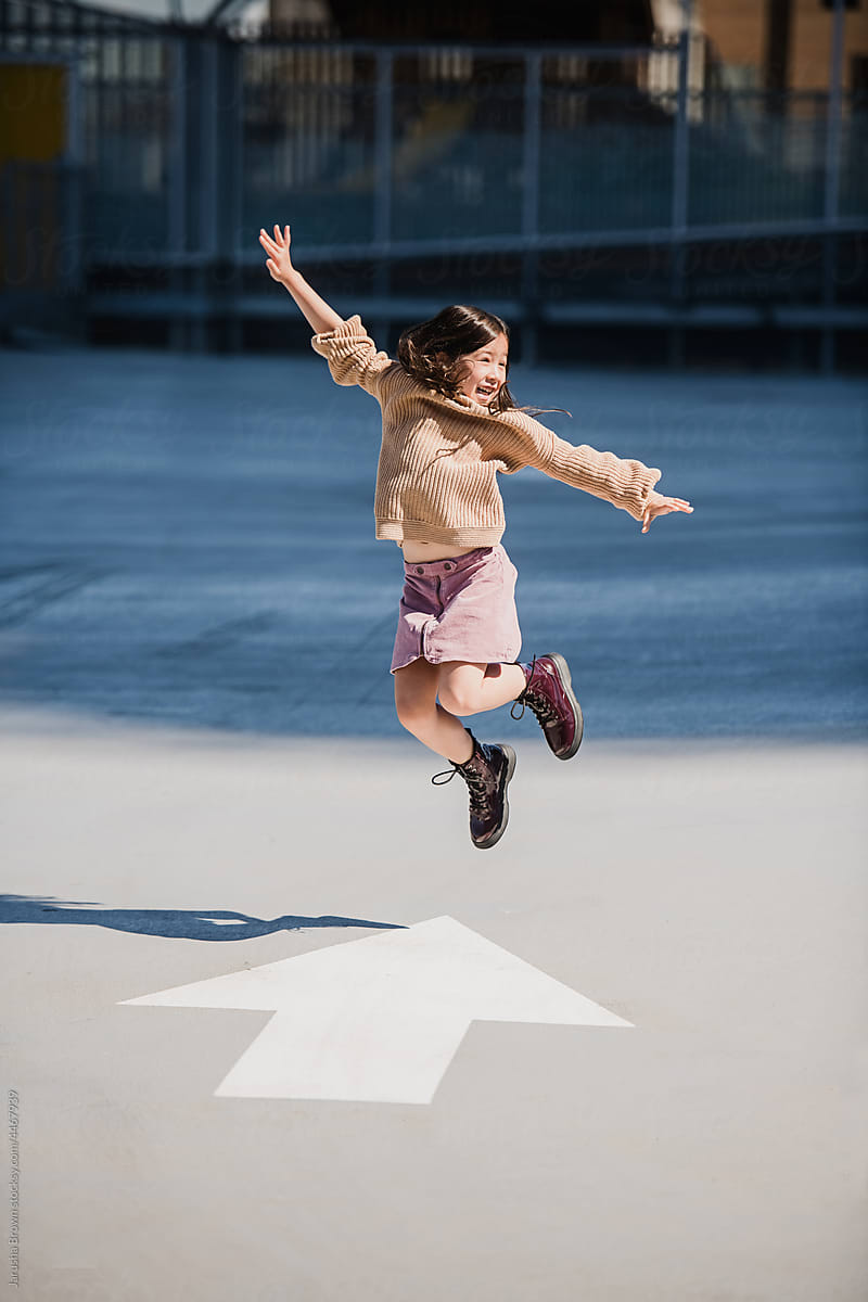 Young girl jumps over a painted arrow on the pavement.