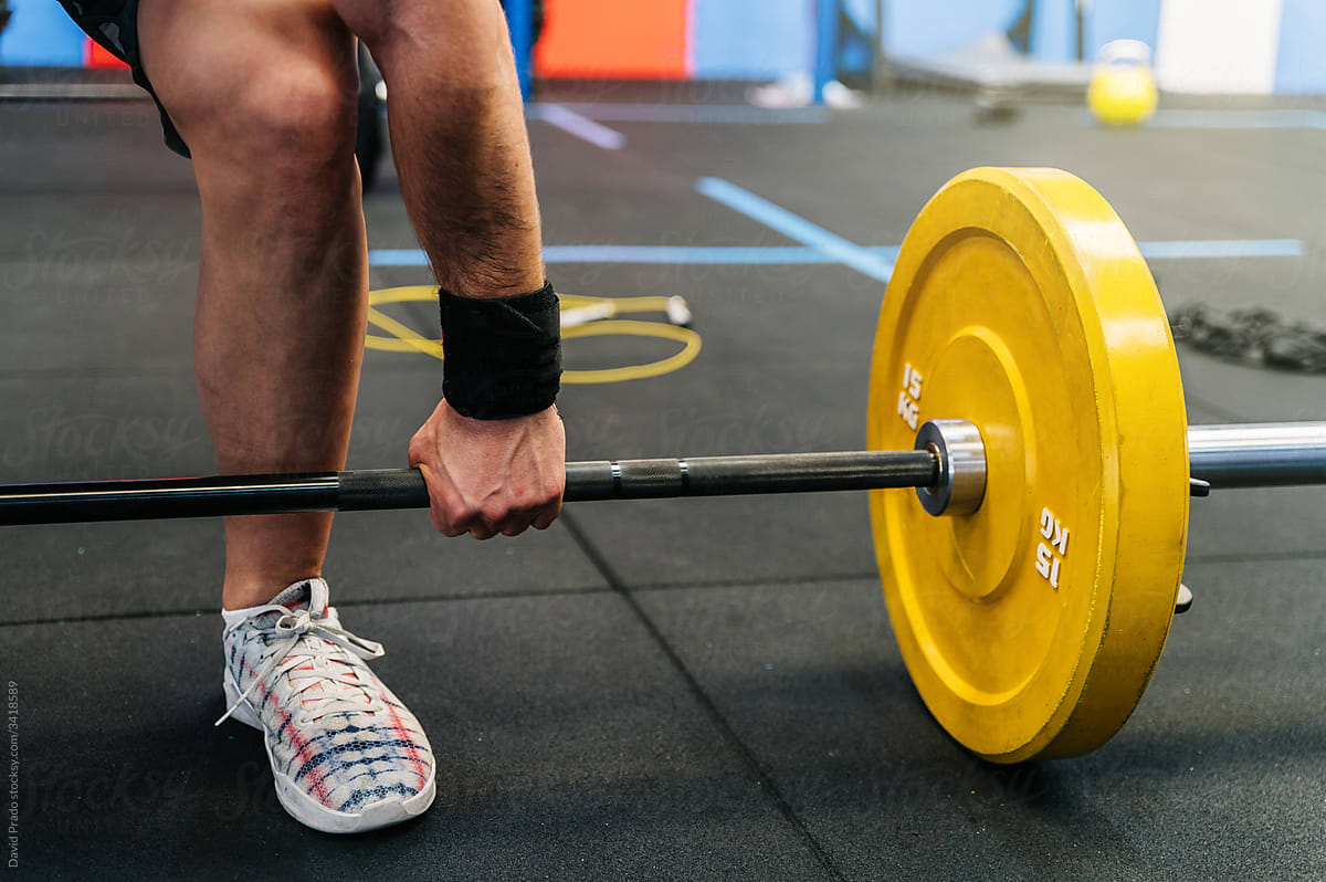 Unrecognizable male athlete lifting barbell from floor