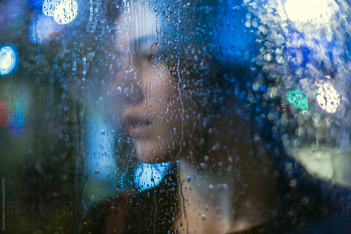 portrait silhouette of a sad girl through the glass with raindrops on it and beautiful bokeh during the rain