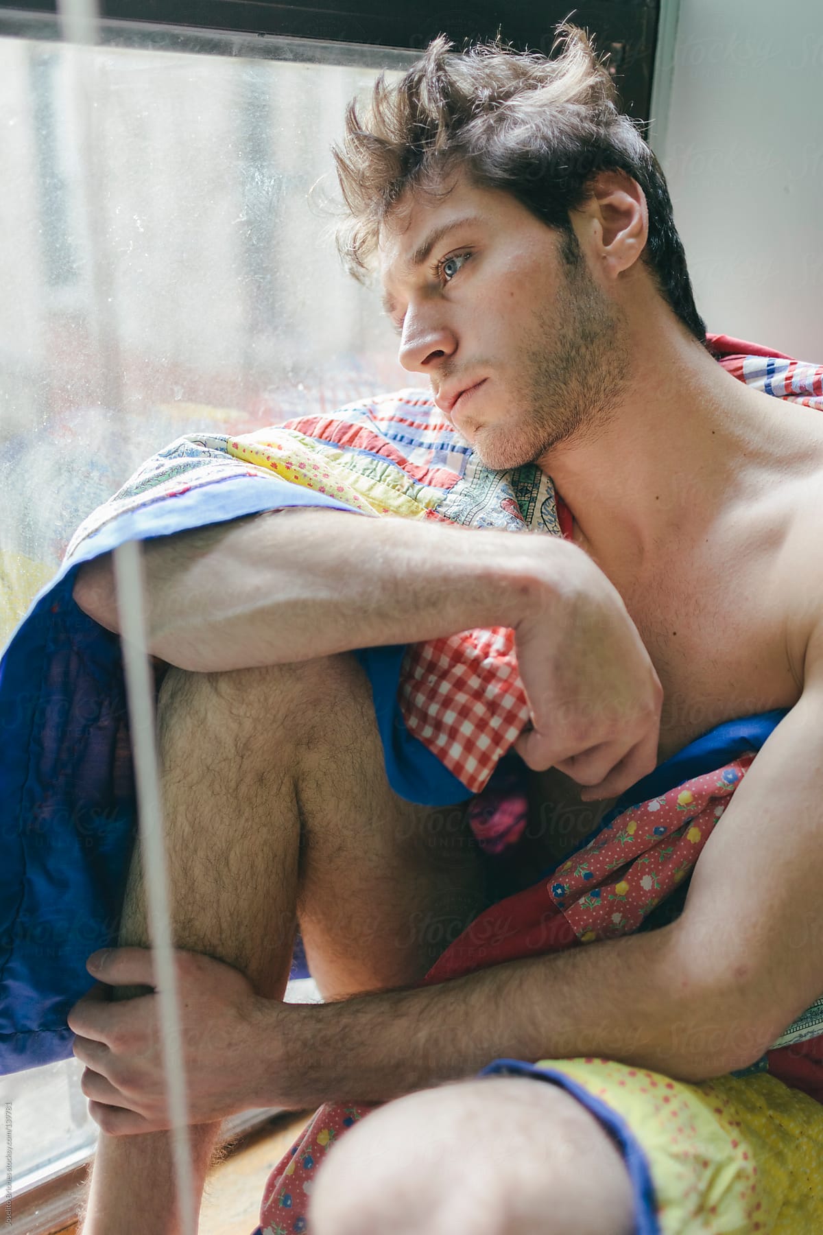 Young Man Waking Up in the Morning Sitting by Window with Quilt