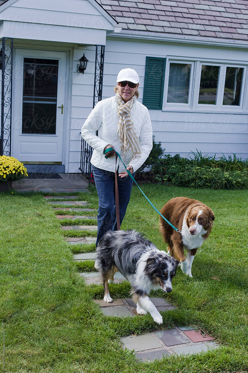 A woman walks her dogs down the front walkway to her house.