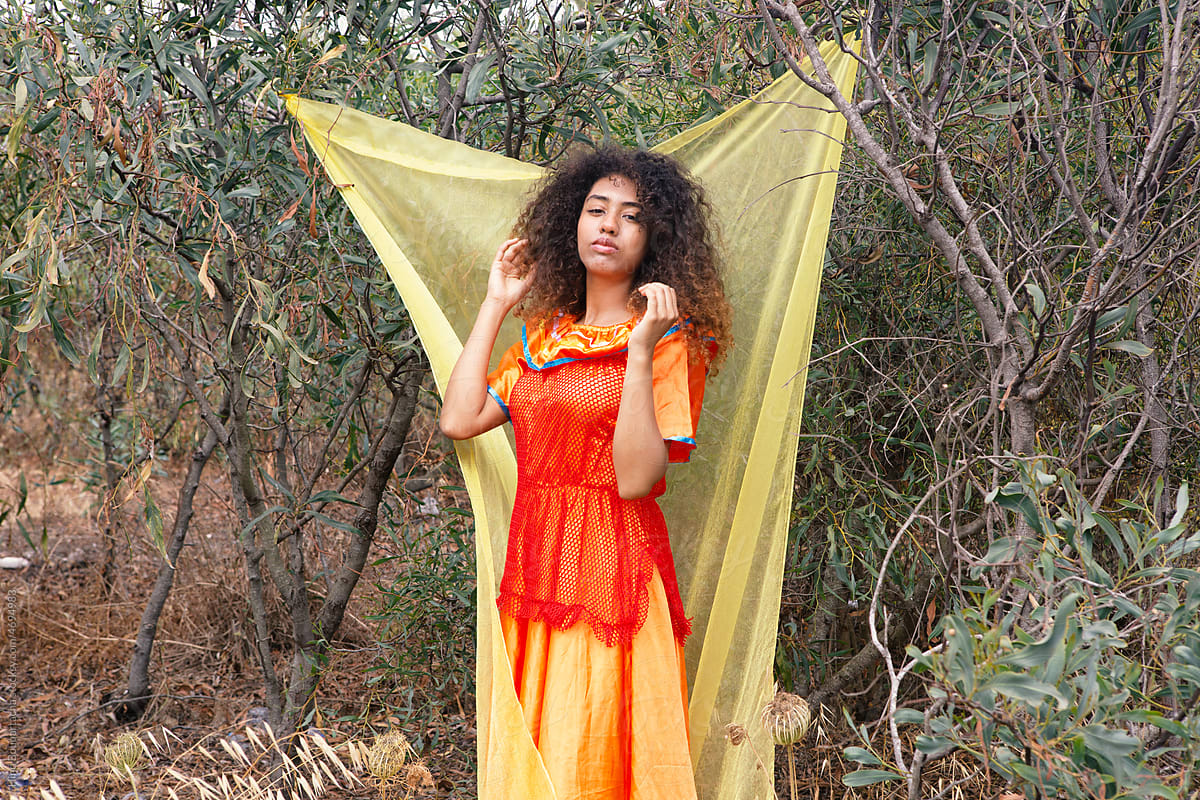 Girl with curly hair wearing orange dress in front of yellow backdrop