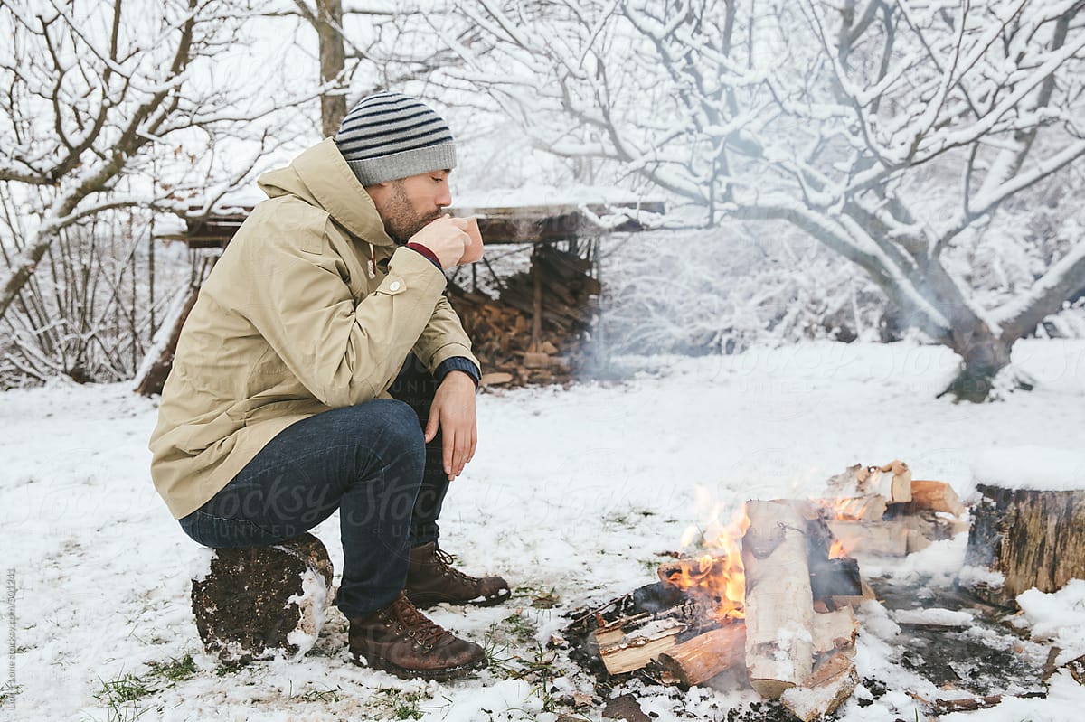 Man drinking hot drink next to bonfire in the snow