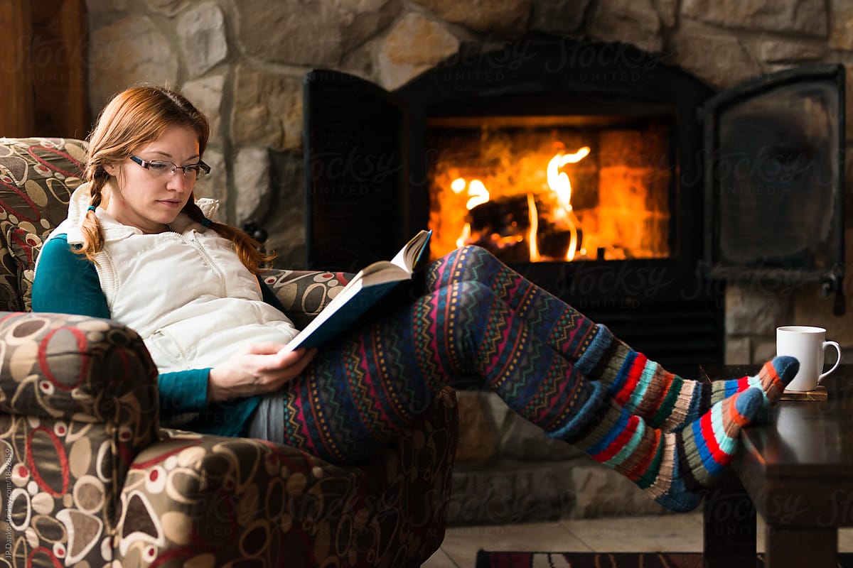 Woman reading by fireplace relaxing on ski vacation