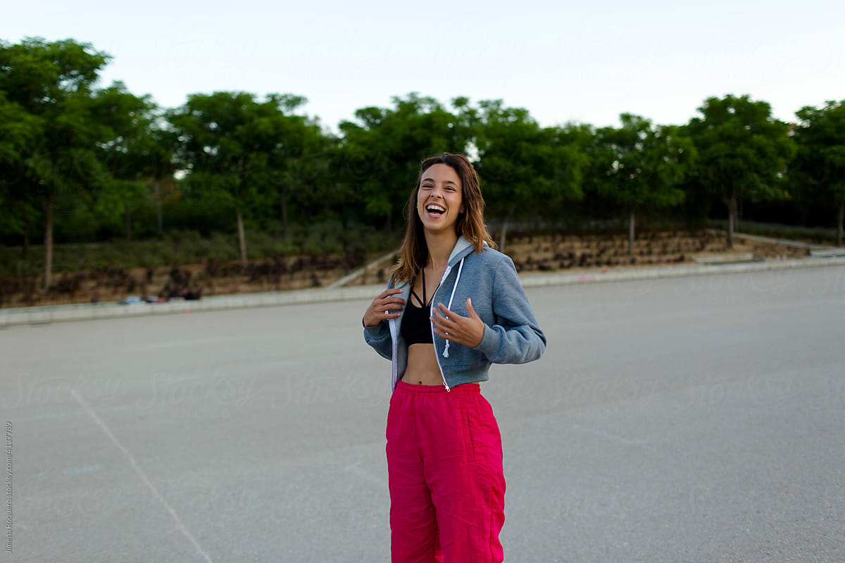 Young woman in sportswear laughing at camera outdoors